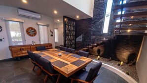A modern dining area with a large wooden table, black upholstered chairs, and a stone wall backdrop. - Casa Picos Palace with swimming pool and panoramic ocean view in Huatulco Bays (Santa María Huatulco)