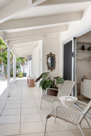 A covered outdoor seating area with two wicker chairs, a potted plant, and a decorative mirror on the wall.