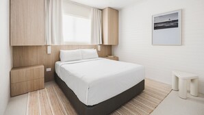 Une chambre d’hôtel moderne, équipée d’un lit, de tables de chevet, d’un ventilateur de plafond et d’un tableau encadré au mur.