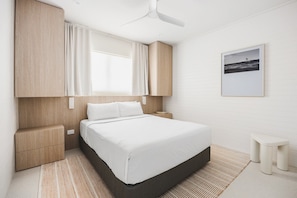 A modern hotel room with a bed, bedside tables, a ceiling fan, and a framed picture on the wall.