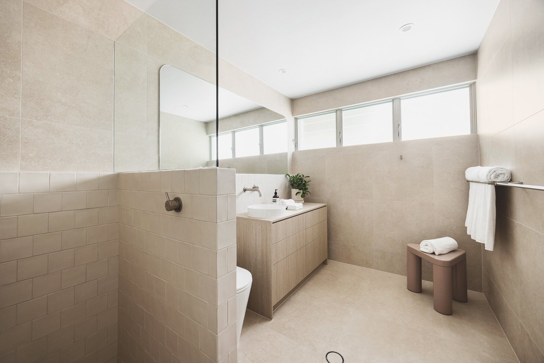 Ein modernes Badezimmer mit Dusche, Toilette, Waschbecken und einem kleinen Hocker.
