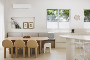 A modern kitchen with a dining area, featuring a round table with chairs, a bench, and a small stool.
