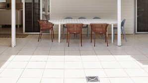Une maison moderne dotée d’un patio couvert, d’une table à manger avec des chaises et d’un coin cuisine.