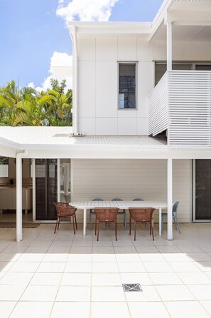 A modern house with a covered patio, a dining table with chairs, and a kitchen area.