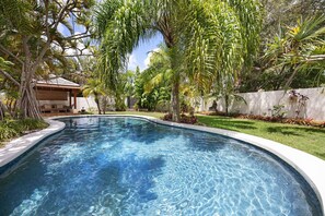 A swimming pool with clear water, surrounded by lush greenery and a white wall.