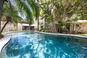 Una piscina rodeada de exuberante vegetación y un edificio moderno con grandes ventanales.