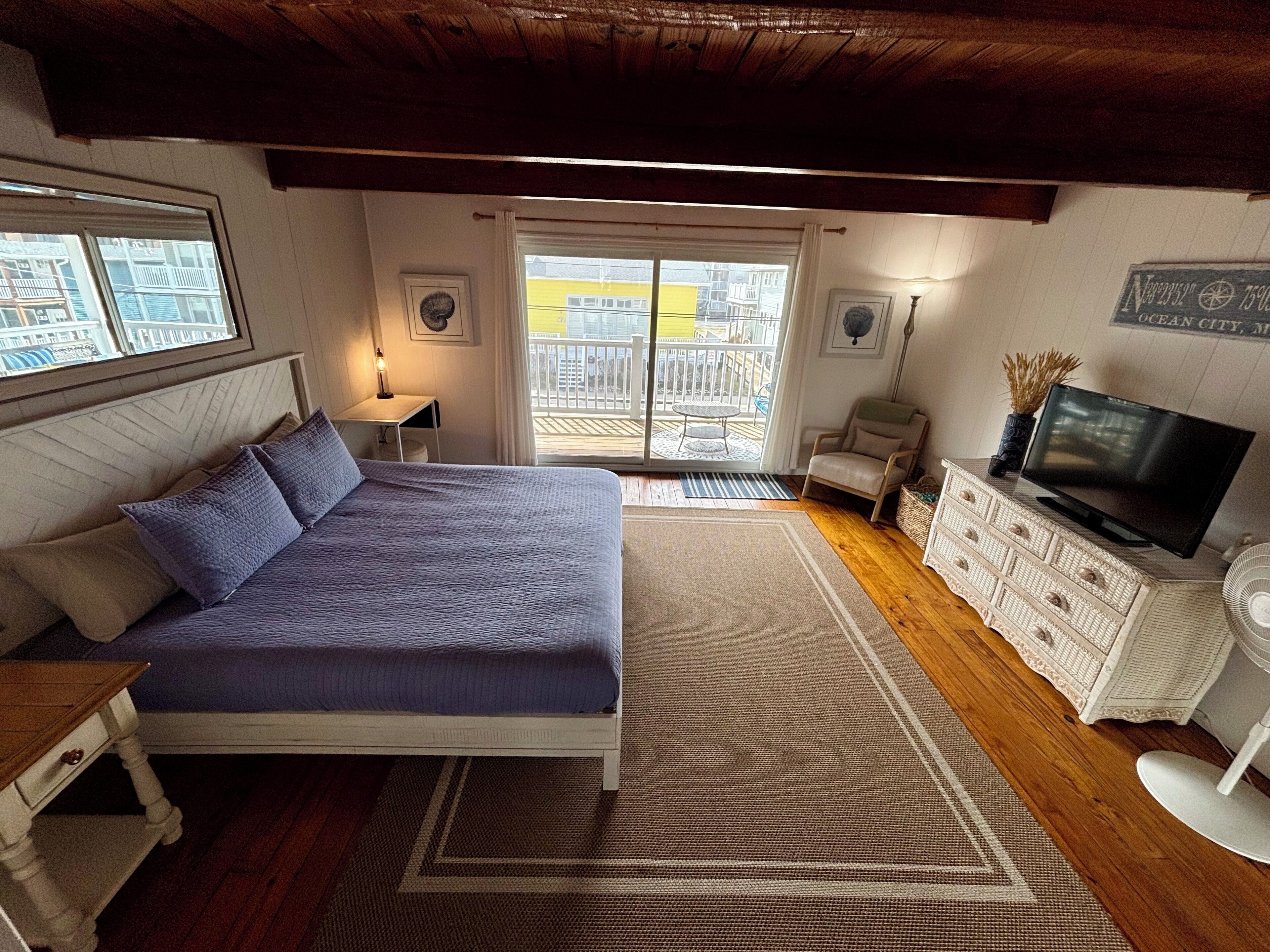 A bedroom with a bed, a dresser, a TV, and a balcony with a view of buildings.