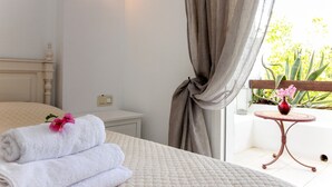 Een slaapkamer met een bed, een nachtkastje, een klein rond tafeltje met een bloevas en uitzicht op groen buiten.