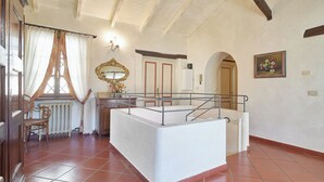 Ein geräumiges Zimmer mit hoher Decke, einer weißen Badewanne und einem Holzstuhl.