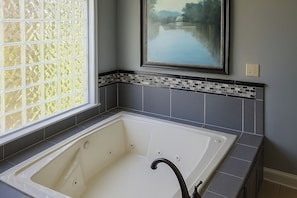 A bathroom with a large bathtub, a window with frosted glass, and a decorative tile border. - Luxury Lakefront 4br: Jacuzzi, Game Room & Wi-fi (Gilbert)