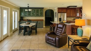 Un salón espacioso con un sillón de cuero, un comedor con mesa y sillas, y una cocina con armarios de madera y un refrigerador.