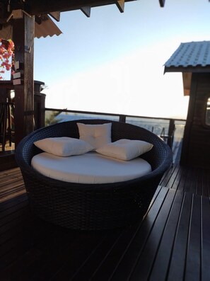 A wicker lounge chair with cushions on a wooden deck.