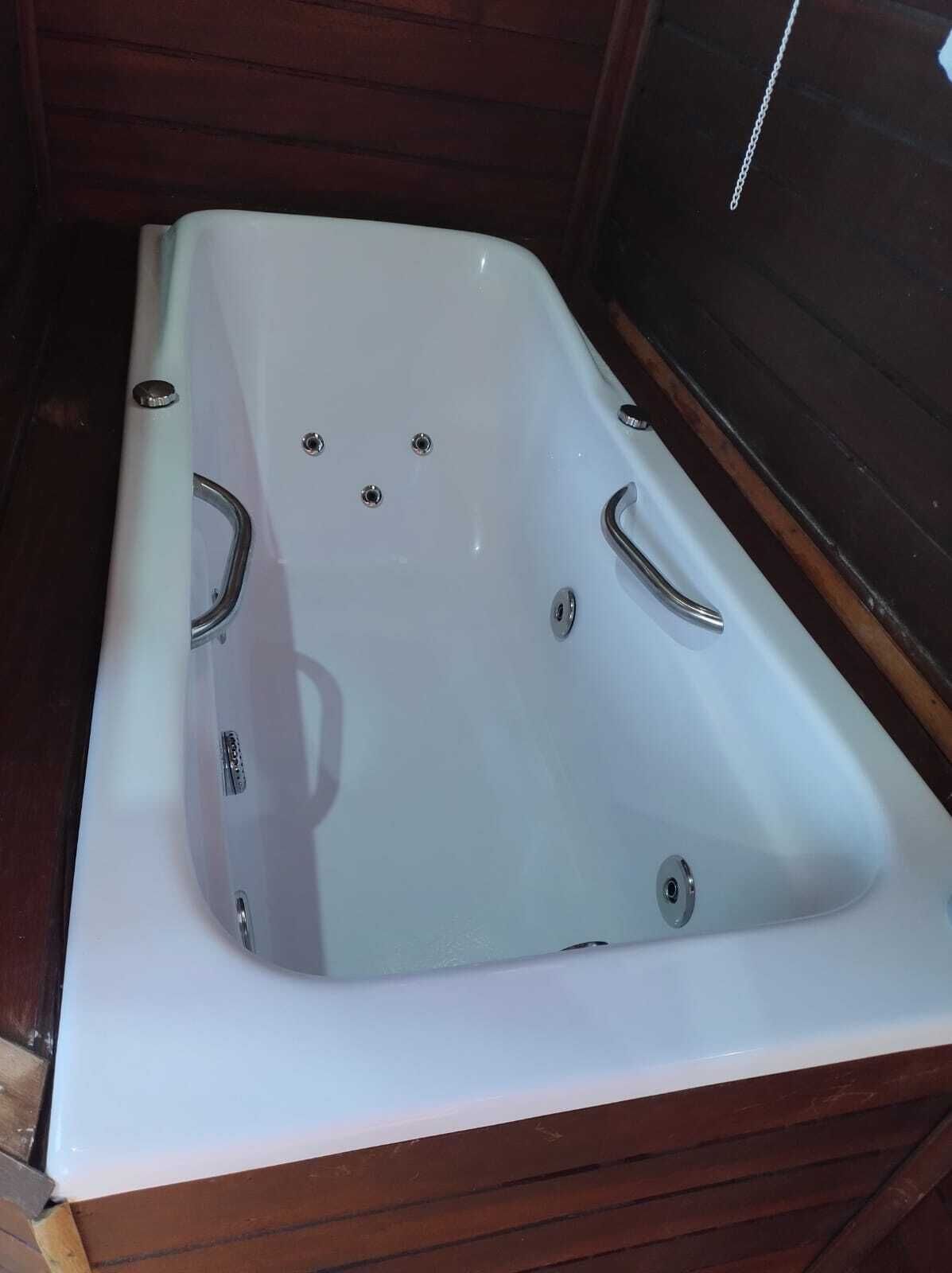 Una bañera blanca con dos grifos y un desagüe, frente a una pared de madera.