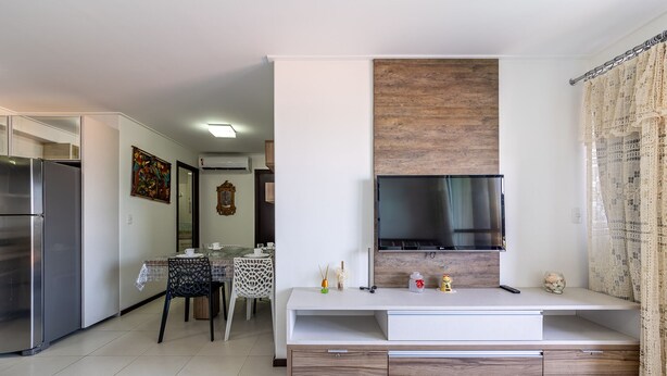 A modern kitchen with a built-in refrigerator, a dining area with a table and chairs, and a flat-screen TV mounted on the wall. - APTO Vista Beira-Mar | Pé na Areia | Barra Bali | Destino BSM 214 (Barra de São Miguel)