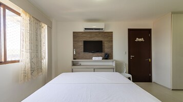 Hotelkamer met een bed, een tv bevestigd aan een houten paneel, een bureau met een ventilator, en een deur met de tekst 'Beach'.