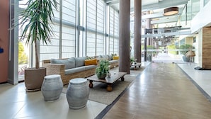 Un espacio interior amplio con un ventanal grande, un sofá con cojines, una mesa de centro y macetas decorativas.