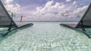 An infinity pool with clear water, two lounge chairs, and a view of the ocean under a partly cloudy sky. - APTO Vista Beira-Mar | Pé na Areia | Barra Bali | Destino BSM 214 (Barra de São Miguel)