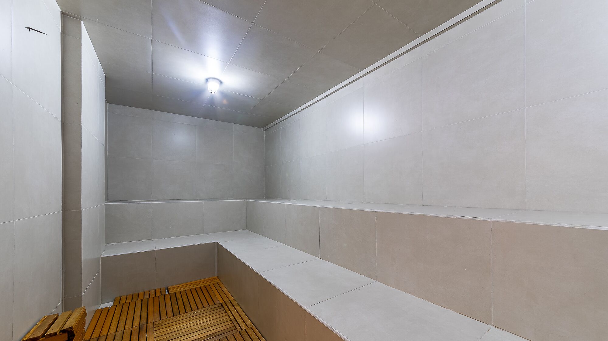 A modern, empty room with white tiled walls and a wooden bench.