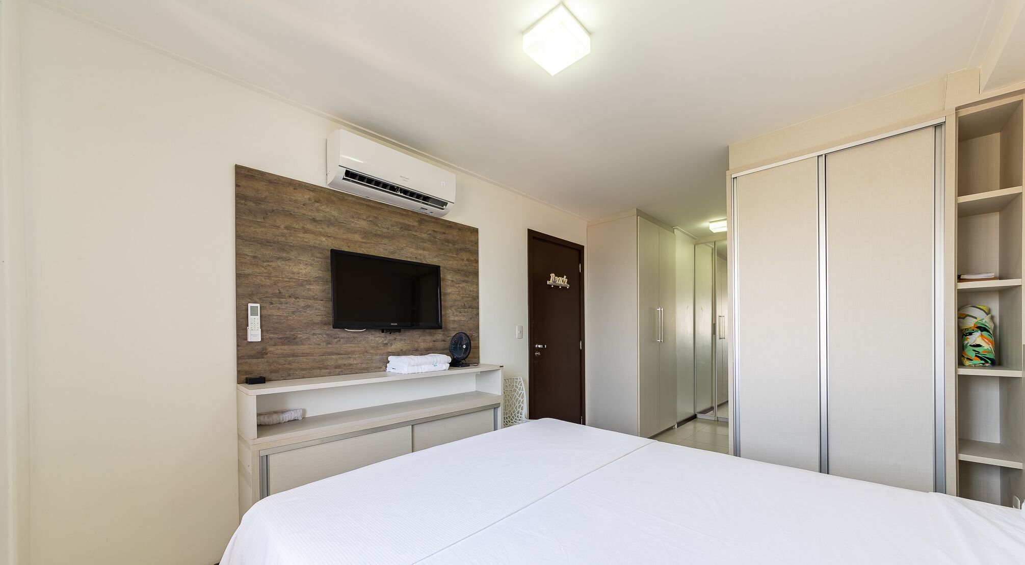 A hotel room with a bed, a TV mounted on a wooden panel, a wardrobe, and a door labeled "Rendezvous".