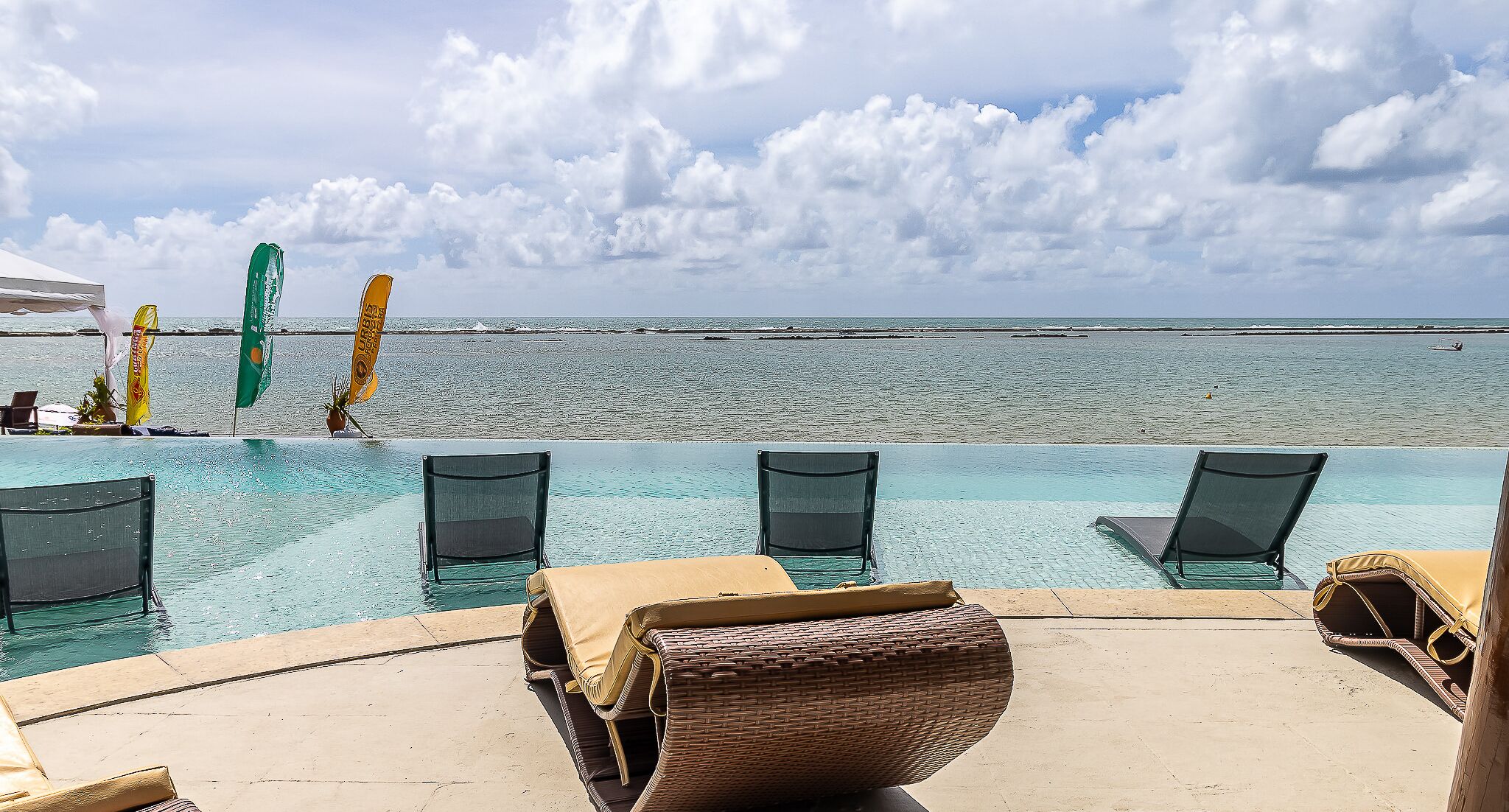An infinity pool with clear blue water, lounge chairs, and a view of the ocean.