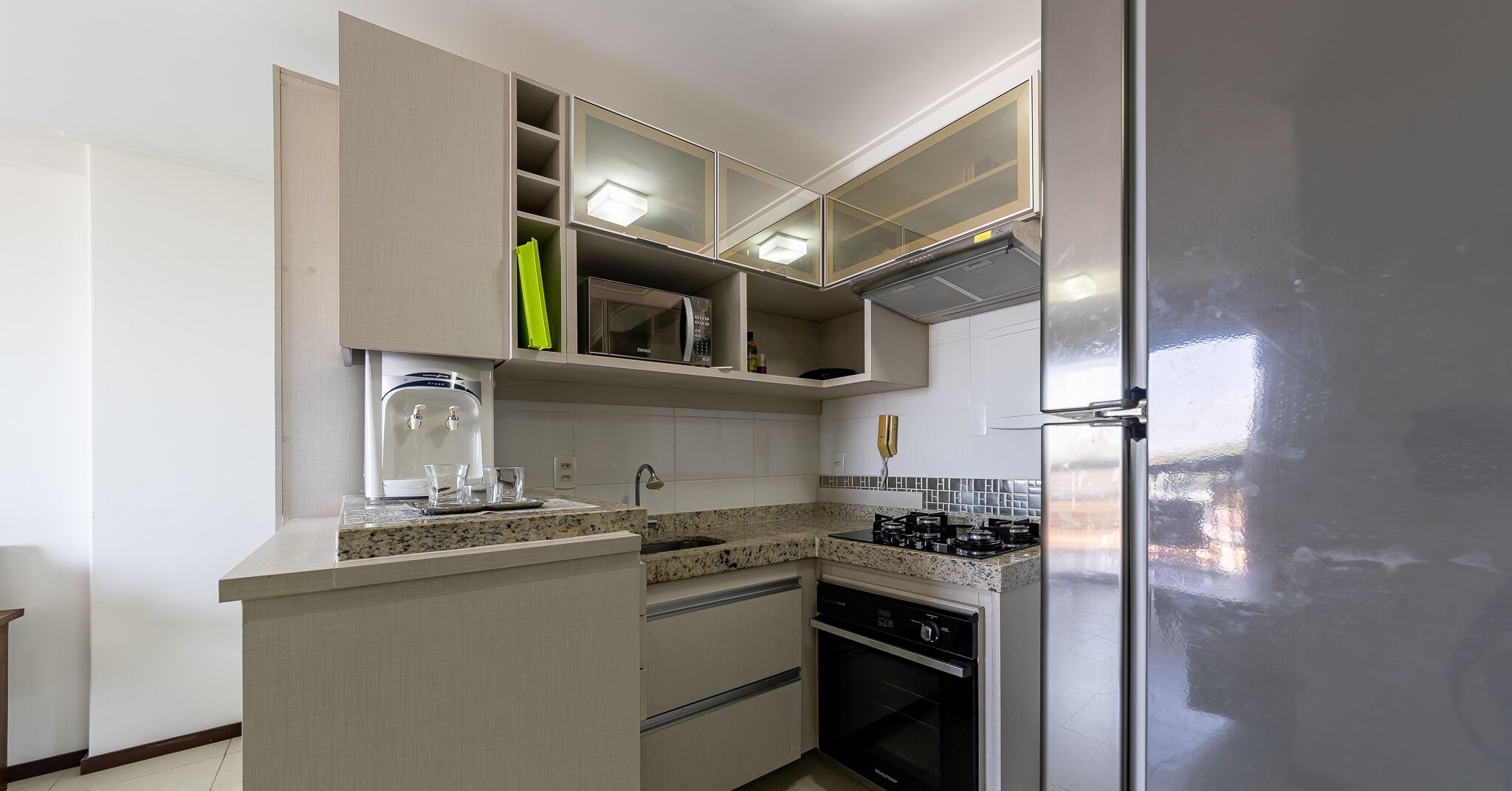 Una cocina compacta con microondas integrado, dispensador de agua, estufa a gas y refrigerador de acero inoxidable.