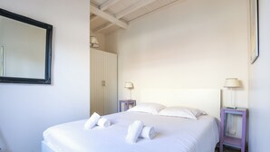 A neatly made bed with white linens and towels, a bedside table with a lamp, and a wardrobe in a simple, clean room. - Maison Fantasio - Welkeys (Dolus-d'Oléron)