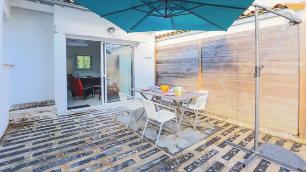 An outdoor patio area with a table and chairs, a large umbrella, and a wooden fence. - Maison Fantasio - Welkeys (Dolus-d'Oléron)