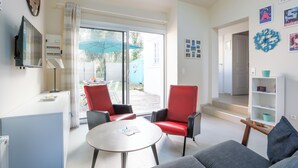 A modern living room with a sofa, two red chairs, a small round table, and a TV mounted on the wall. - Maison Fantasio - Welkeys (Dolus-d'Oléron)