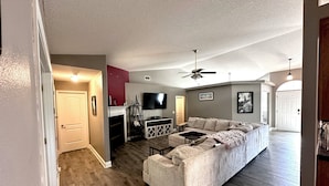 A spacious living room with a sectional sofa, a fireplace, a ceiling fan, and a TV mounted on the wall. - Forget your worries in this spacious and serene space with a beautiful lake view (Milton)