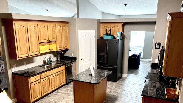 A modern kitchen with wooden cabinets, a black refrigerator, and a granite countertop. - Forget your worries in this spacious and serene space with a beautiful lake view (Milton)