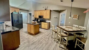 A kitchen with wooden cabinets, a refrigerator, a microwave, and a dining area with a table and chairs. - Forget your worries in this spacious and serene space with a beautiful lake view (Milton)