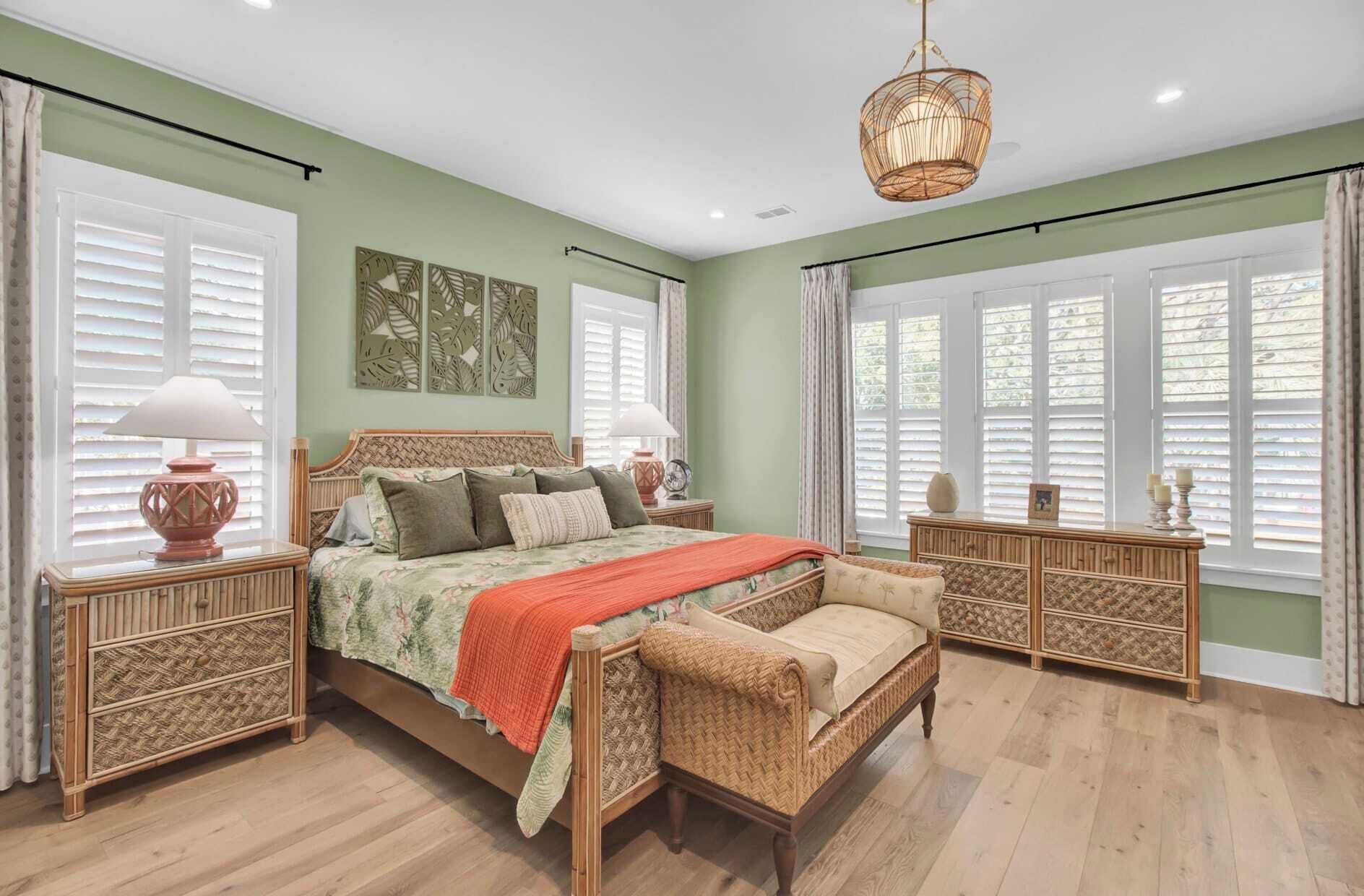 A bedroom with a bed, bedside tables, a chair, a dresser, and a large window with blinds.