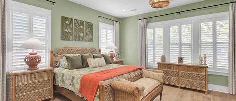 A bedroom with a bed, bedside tables, a chair, a dresser, and a large window with blinds.