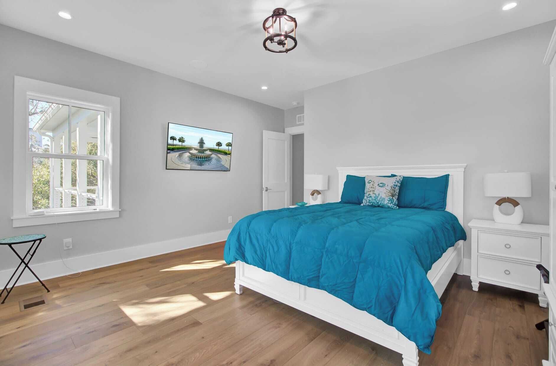 Une chambre à coucher avec un grand lit, des tables de chevet blanches, un tableau au mur et une fenêtre avec des stores.