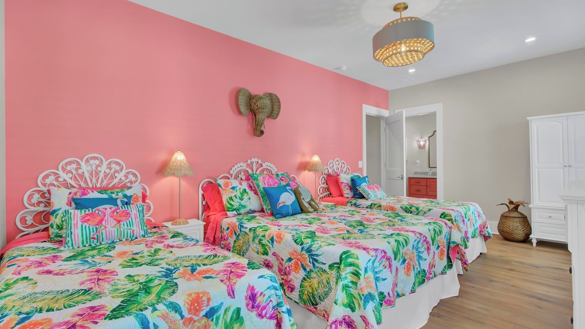 A bedroom with two beds, a pink wall, and a ceiling light.