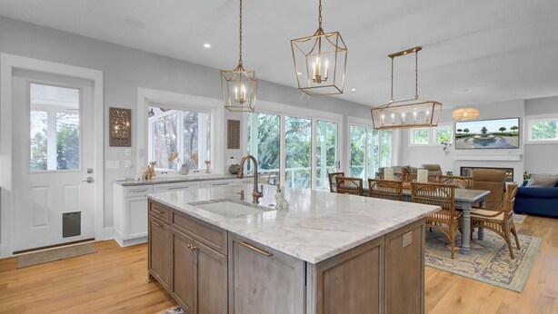 A spacious kitchen with a large island, pendant lighting, and a dining area with wicker furniture.