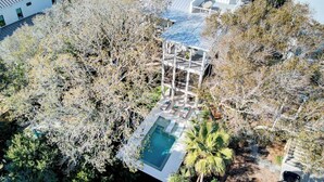An aerial view of a residential property with a swimming pool, a covered outdoor area, and surrounding trees.
