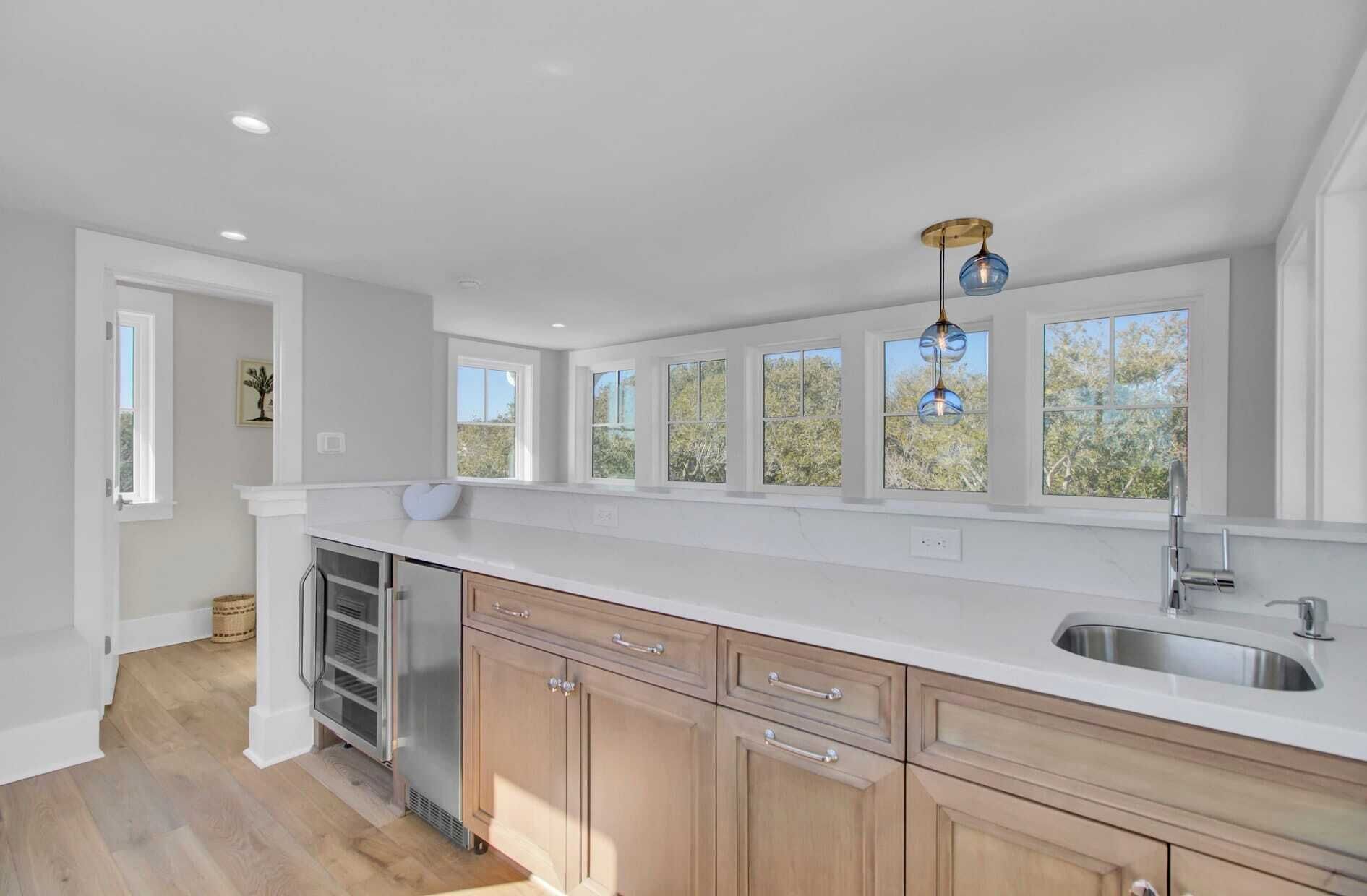 A modern kitchen with a large island, a stainless steel sink, and a window overlooking greenery.