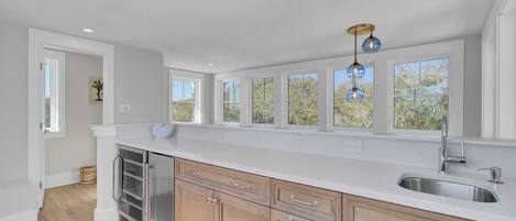 A modern kitchen with a large island, a stainless steel sink, and a window overlooking greenery.