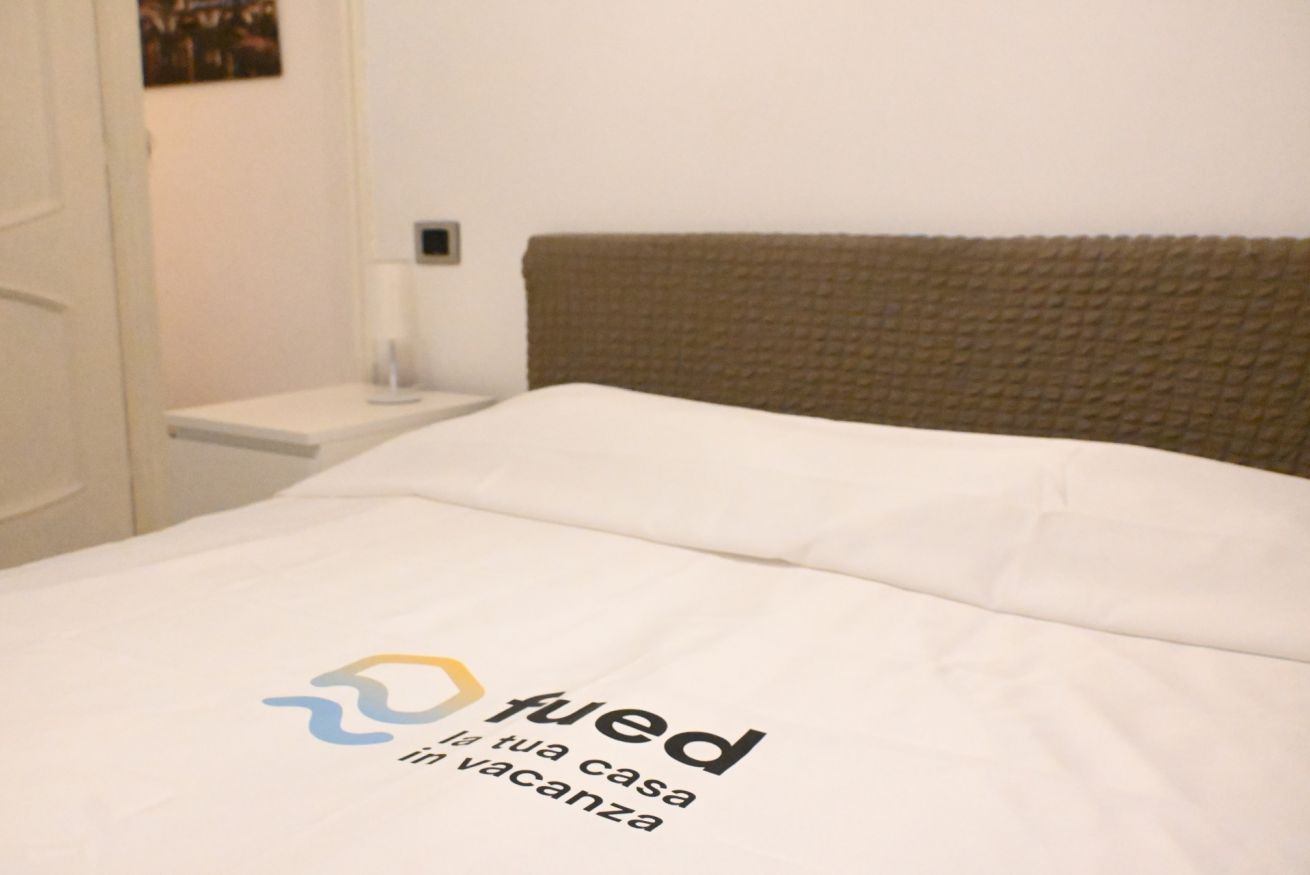 Una cama bien hecha con sábana blanca y un logotipo en el cabecero.