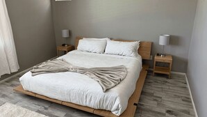 Een opgemaakt bed met een beige plaid, twee nachtkastjes met lampen, en een houten hoofdbord.