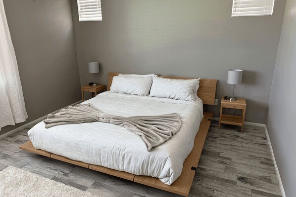 A neatly made bed with a beige throw blanket, two bedside tables with lamps, and a wooden headboard. - Luxe Indio Stay w/ Pool, Tiki Bar & Fire Pit Near Coachella Longfellow (Indio)