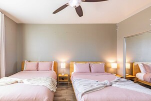 A bedroom with two beds, wooden headboards, bedside lamps, a ceiling fan, and a large mirror on the wall.