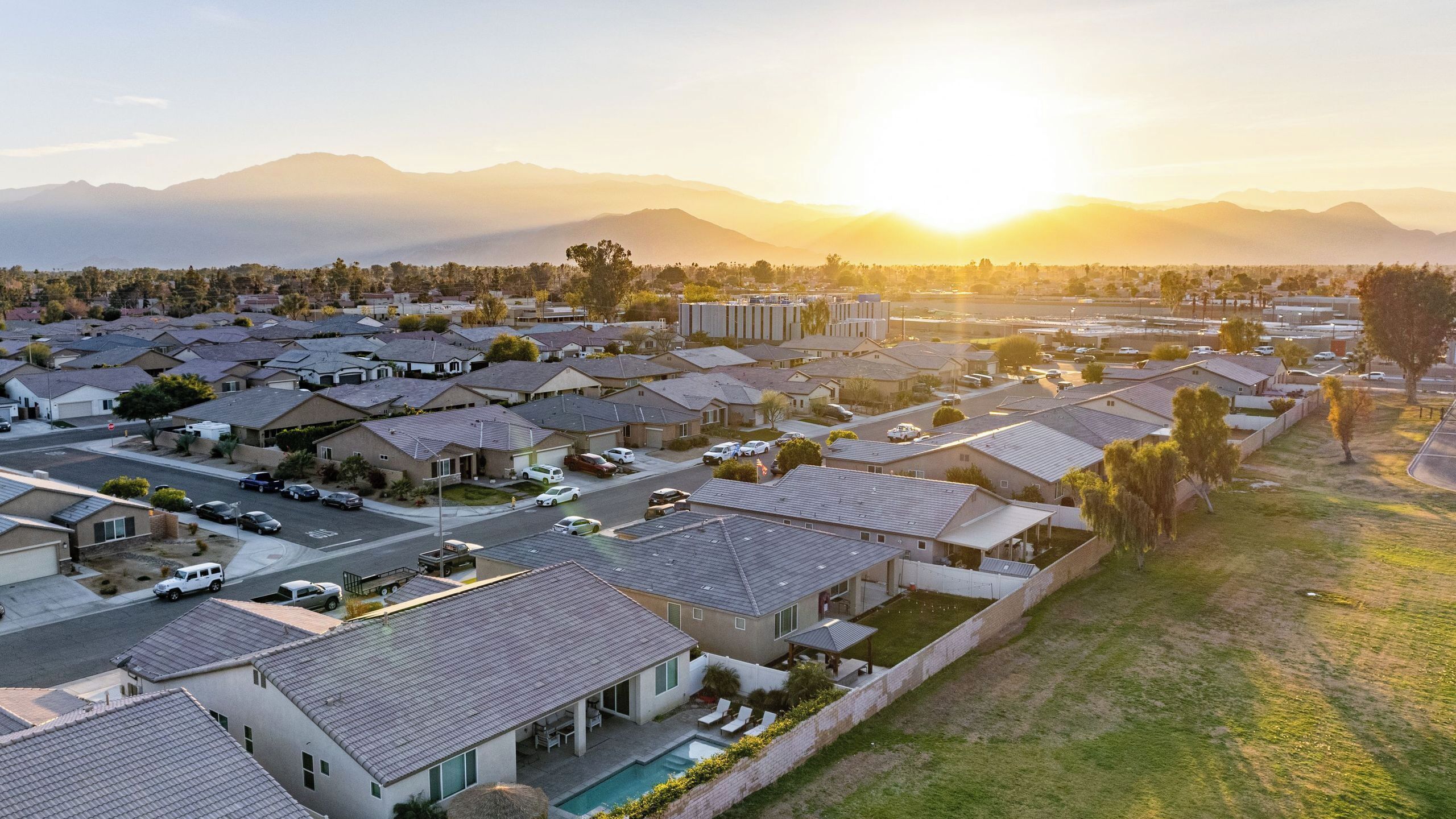 A residential area with houses, a swimming pool, and a mountain range in the background.