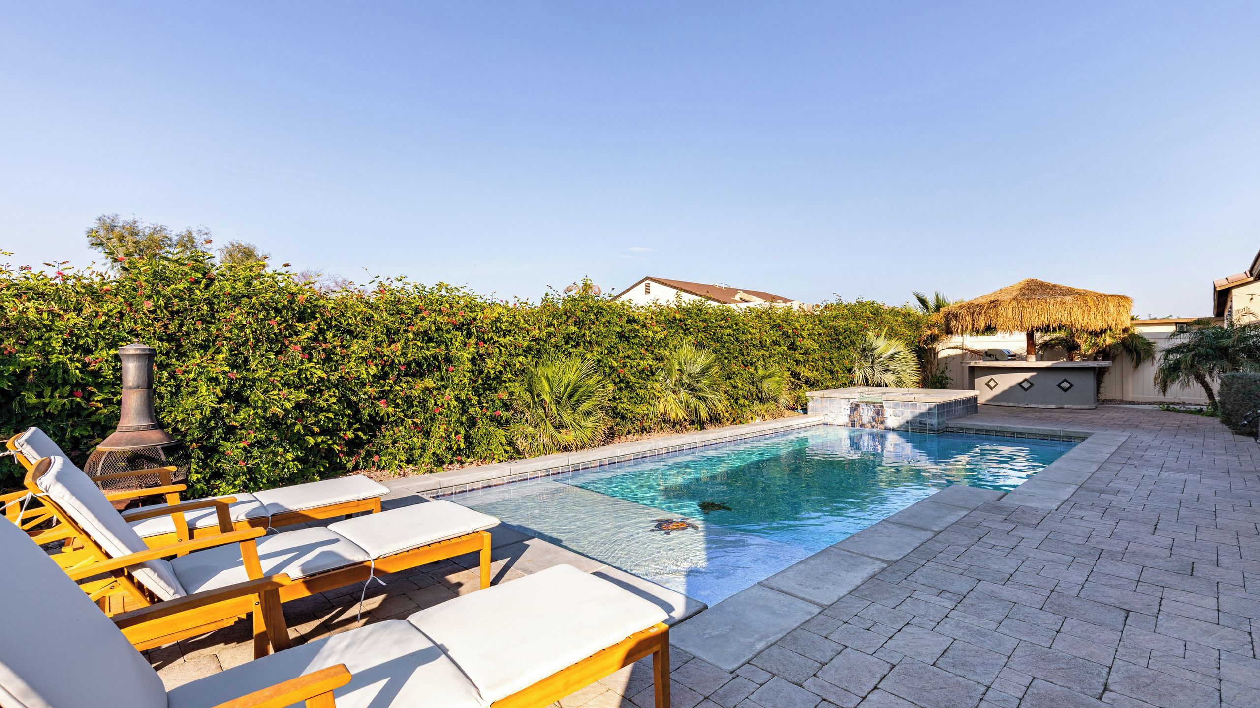 Una piscina con sillones de descanso y una parrilla.