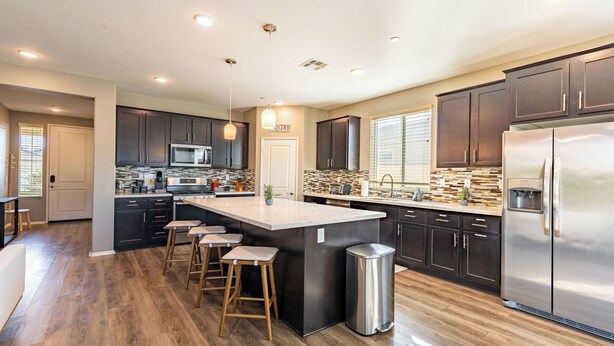 A modern kitchen with dark cabinets, a stainless steel refrigerator, and a central island with stools. - Luxe Indio Stay w/ Pool, Tiki Bar & Fire Pit Near Coachella Longfellow (Indio)