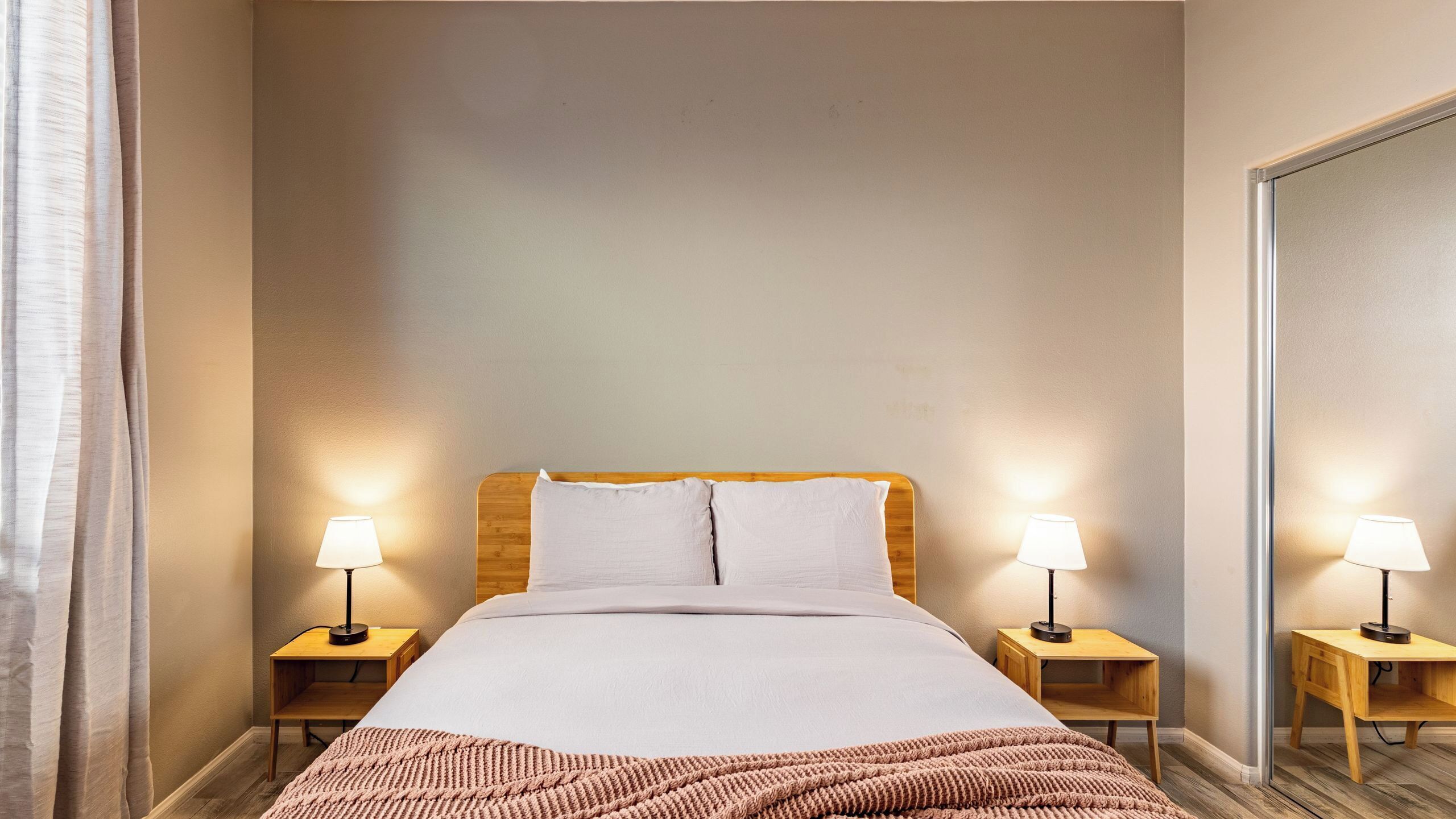 A neatly arranged hotel room with a bed, two bedside tables with lamps, a wooden headboard, and a large mirror on the wall.