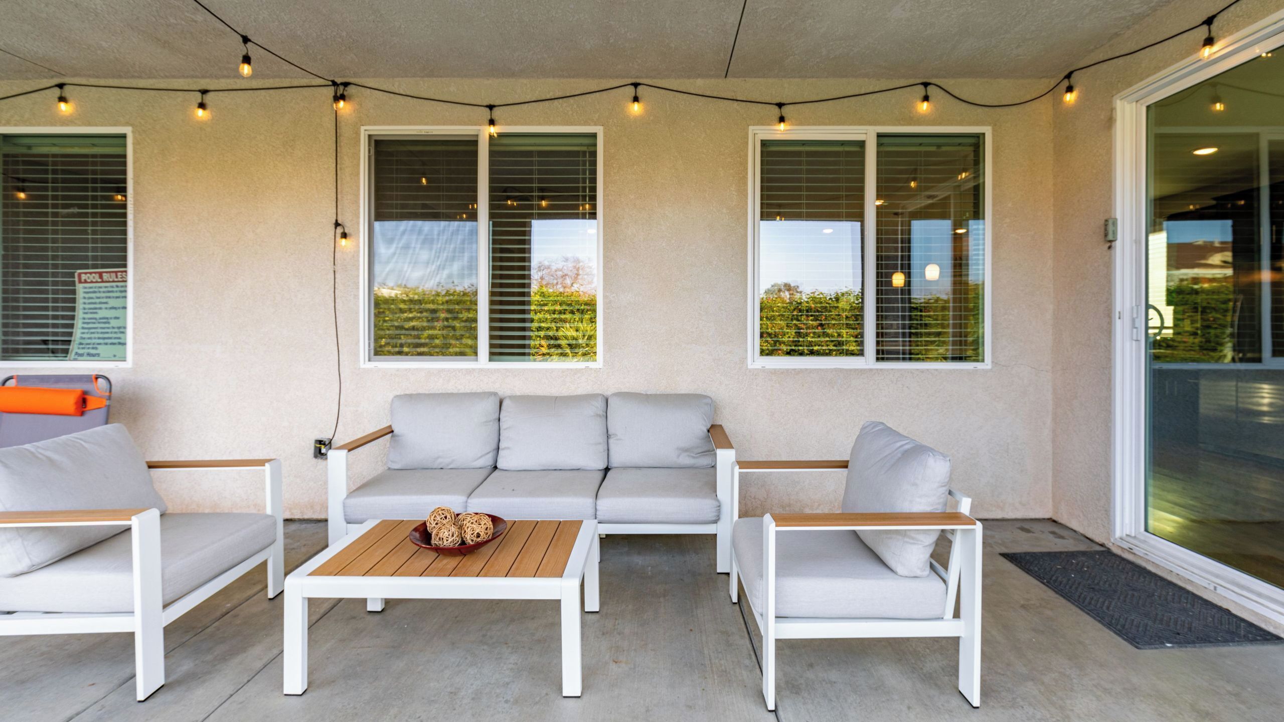 Een overdekt terras met een witte bank, twee witte fauteuils, een houten bijzettafeltje en lichtslingers.