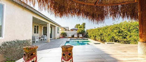 A pool area with tiki statues, a covered patio, and a view of a house with outdoor seating.