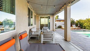 A covered outdoor seating area with chairs and a bench, a pool, and a view of a house. - Luxe Indio Stay w/ Pool, Tiki Bar & Fire Pit Near Coachella Longfellow (Indio)